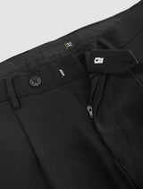 Man wearing black relaxed fit pleated pants with belt loops and side pockets.