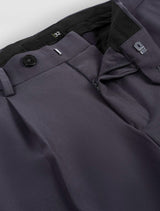 Close-up view of men's charcoal gray wide-leg pleated trousers with a visible button and zipper closure, and pockets.