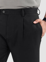 Man wearing black relaxed fit pleated pants with belt loops and side pockets.