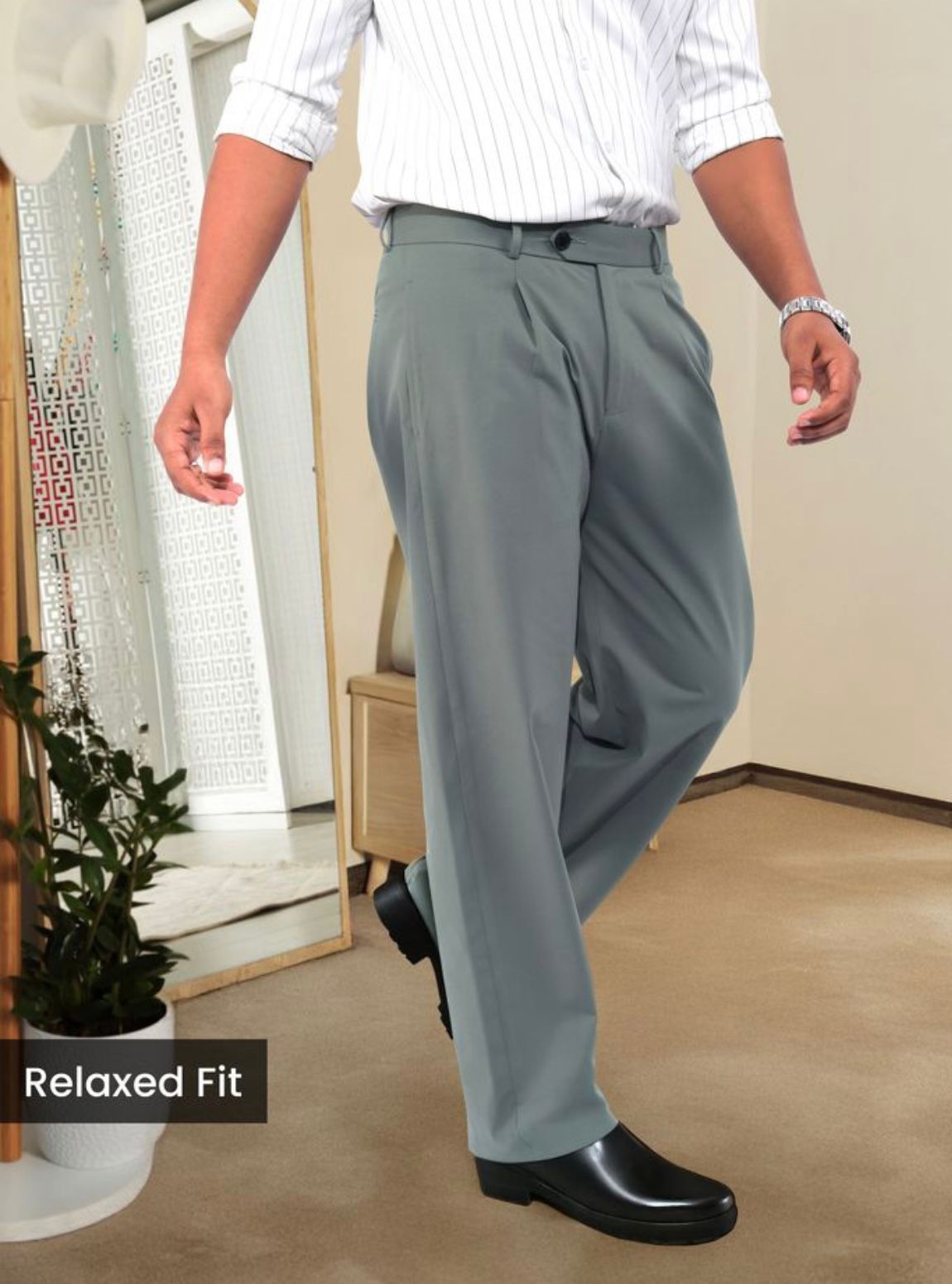Man wearing slate grey relaxed fit pleated trousers with a white striped shirt and black dress shoes.